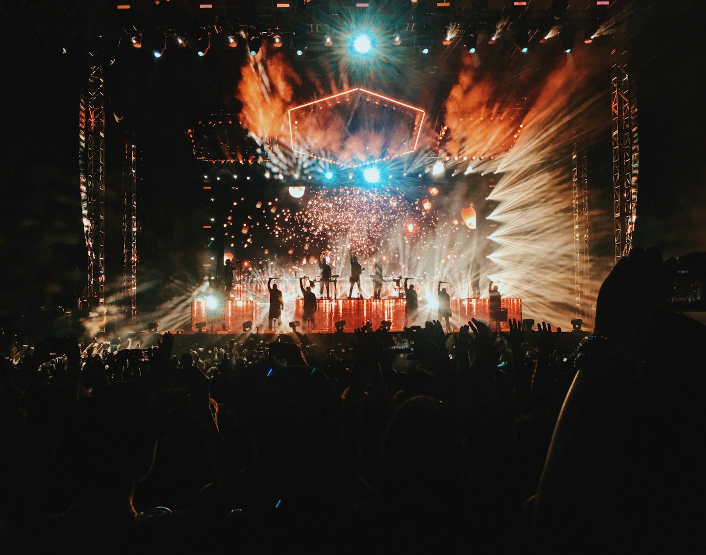 Silhouetted performers on a concert stage with pyrotechnics and lanterns.